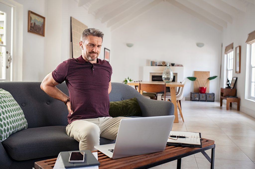 man working from couch with back hurting