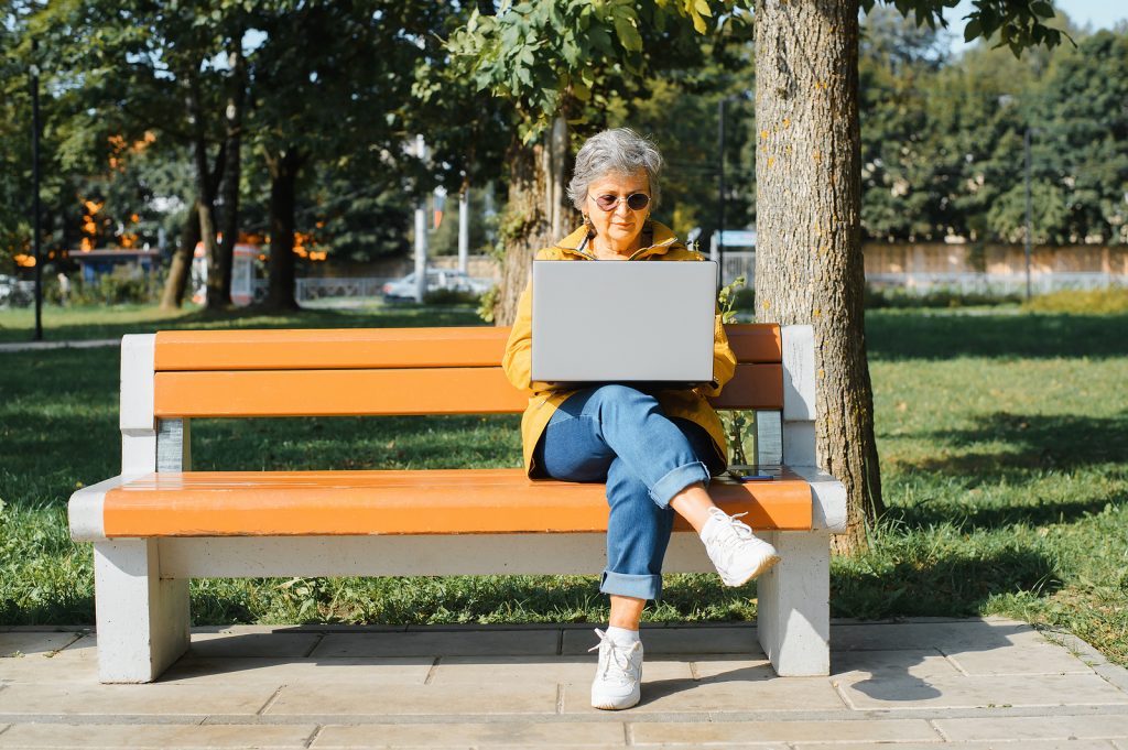 older woman working from laptop on park bench
